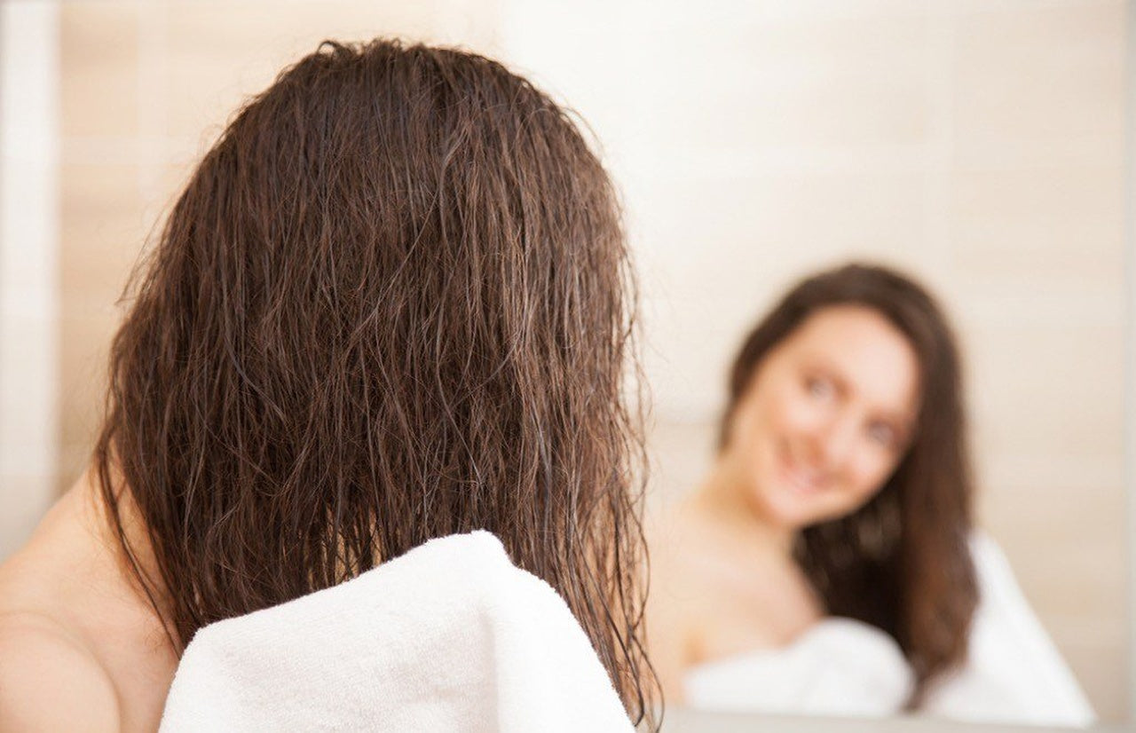 a woman dries her hairs with a white towel in front of the mirror